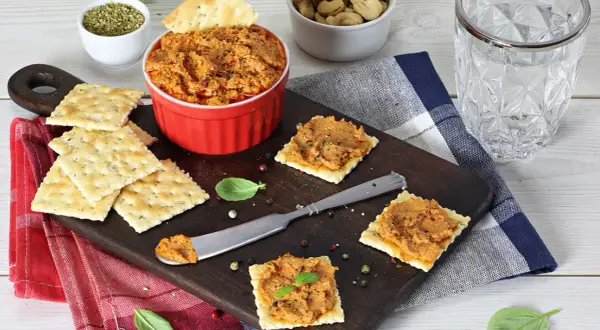 Pasta z suszonych pomidorów na krakersach, podana na desce z dodatkami.
