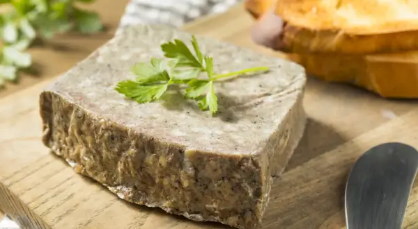 Un bloc de pâté rustique, garni de persil frais, prêt à être tartiné sur des toasts grillés. Un assaisonnement pâté parfait pour un apéritif gourmand.