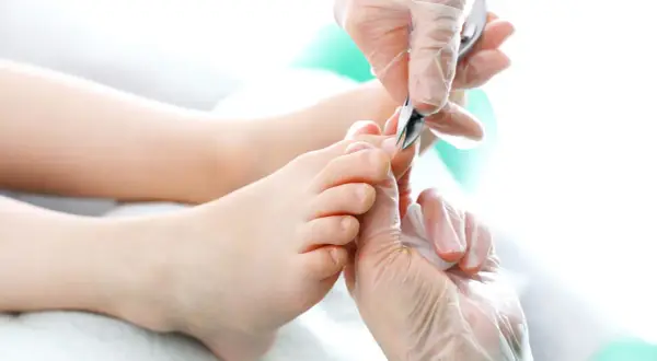 Dłonie w rękawiczkach precyzyjnie przycinają paznokcie u nóg. Pedicure w toku, dbałość o każdy szczegół.