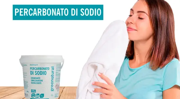 Donna annusa un candido asciugamano, felice del profumo fresco. Accanto, un barattolo di Percarbonato di Sodio, smacchiatore naturale per lavatrice.