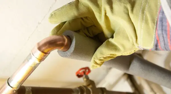 Mit gelben Handschuhen werden Heizungsrohre isoliert, um Energie zu sparen.