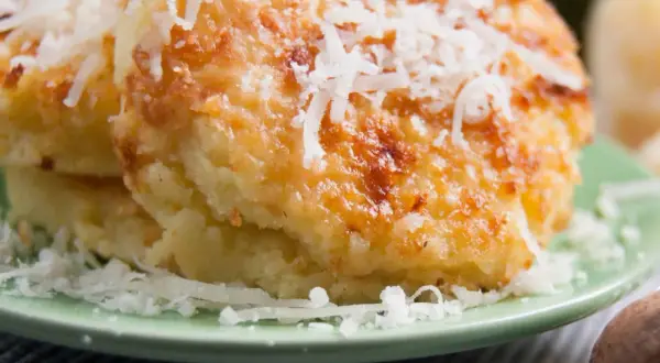 Gebackene Gnocchi alla Romana, goldbraun und mit geriebenem Parmesan bestreut, auf einem grünen Teller.