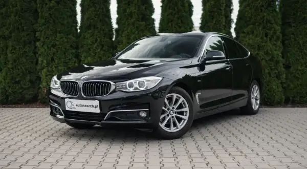 Eleganckie, czarne BMW GT lśni na tle zielonych drzew.