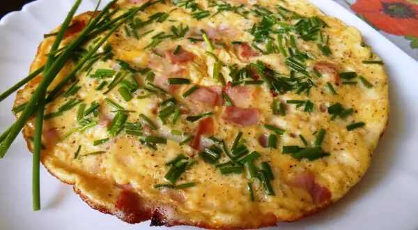 Puszysty omlet ze szczypiorkiem i kawałkami wędliny, podany na białym talerzu.