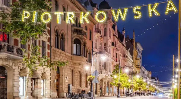 Ulica Piotrkowska nocą, iluminowana neonami i girlandami świateł. Idealne miejsce, by poczuć klimat Łodzi i zastanowić się, co zwiedzić w Łodzi.