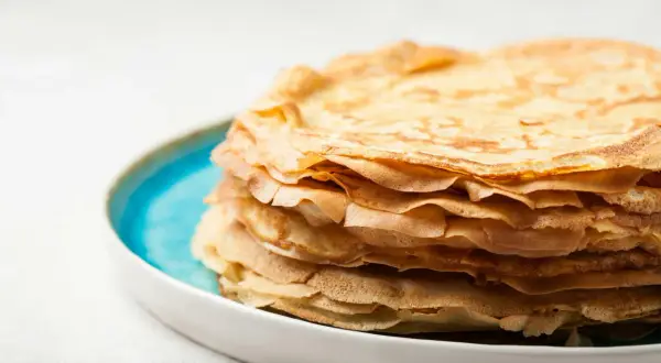 En hög med gyllene pannkakor, gjorda med vatten istället för mjölk, ligger på en blå och vit tallrik.