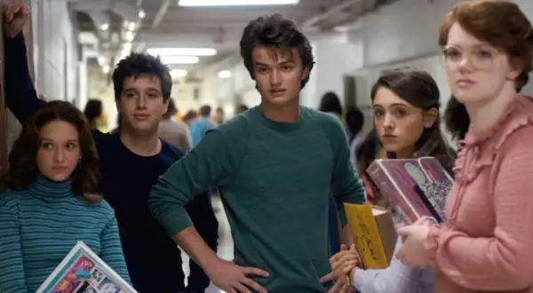 A group of teens in a hallway, featuring the iconic Stranger Things color palette of muted blues, greens, and pinks.