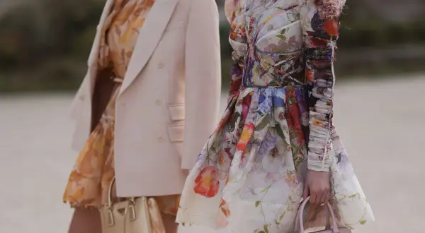 Jasny żakiet do sukienki w kwiaty to świetny wybór. Dwie kobiety prezentują stylizacje z kwiecistymi sukienkami i eleganckimi torebkami.