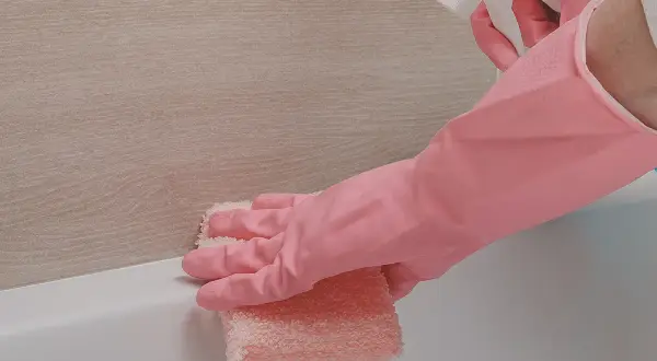 Main rose, une éponge rose nettoie le joint silicone jauni de la baignoire.