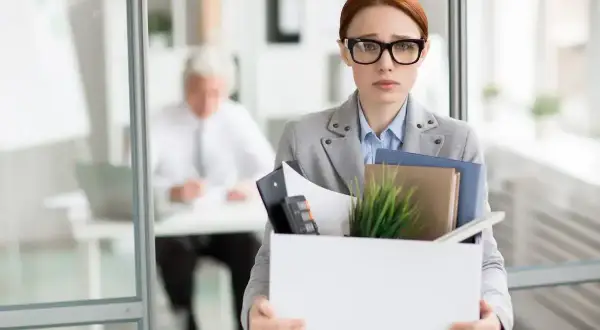 Smutna kobieta z pudełkiem rzeczy po likwidacji stanowiska pracy. Czy otrzyma należną odprawę?