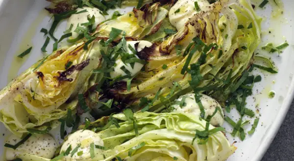 Ugnsbakad vitkål, skuren i klyftor, serverad med en krämig dressing och färska örter. En enkel men smakrik rätt.