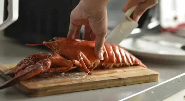 Eine Hand schneidet einen gekochten Hummer auf einem Holzbrett. Die Frage "Hummer kochen wie lange?" wird hier visuell beantwortet.