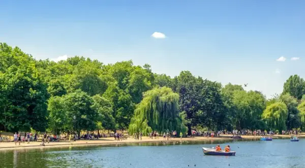 Słoneczny dzień w Hyde Park w Londynie. Ludzie odpoczywają nad jeziorem, niektórzy pływają łódkami.
