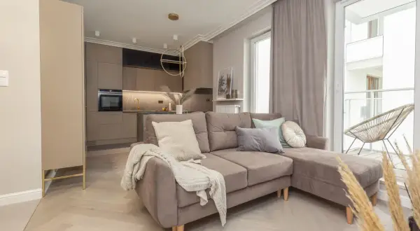 Przytulny salon z aneksem kuchennym w odcieniach beżu i szarości. Dominują tu **kolory monochromatyczne**, tworząc spójną i elegancką przestrzeń.