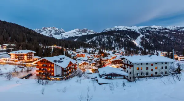 Paesaggio innevato di Madonna di Campiglio al crepuscolo. Hotel illuminati e montagne sullo sfondo, un invito a scoprire cosa vedere.