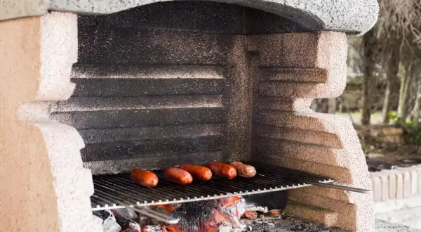 Prosty murowany grill z cegły, na którym pieką się kiełbaski nad żarem.