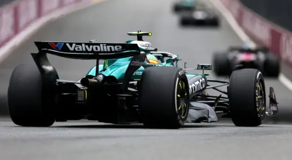 Un coche Aston Martin F1 verde compite en la pista, con otros coches borrosos detrás.