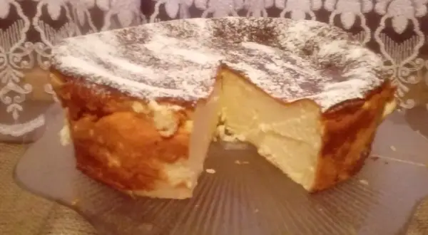 Puszysty sernik z mlekiem skondensowanym, oprószony cukrem pudrem, prezentuje się apetycznie na szklanej paterze.