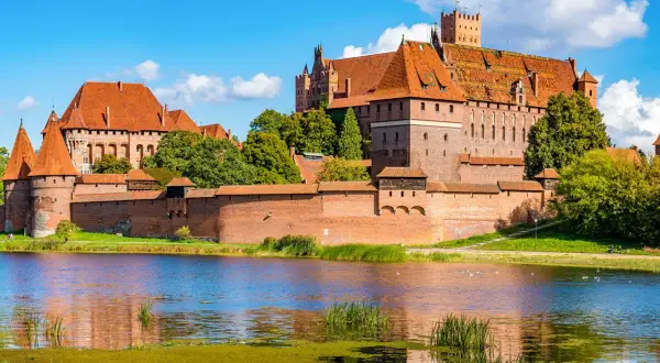 Die imposante Marienburg Burg, eine mittelalterliche Festung aus rotem Backstein, thront über einem ruhigen See.