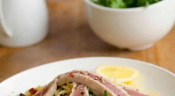 Un piatto di spaghetti con tonno fresco, rucola, capperi e una fetta di limone.