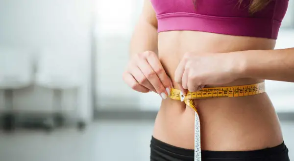 Une femme mesure sa taille avec un mètre ruban. La question "peut on maigrir sans sport" est au cœur de cette image de perte de poids.