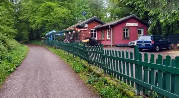 Der Weg zum Bahnhof Burgholz führt vorbei an einer roten Gaststätte mit grünen Zäunen und Autos.