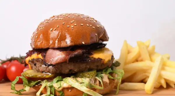Apetyczny burger wołowy z bekonem, serem, warzywami i frytkami na desce.