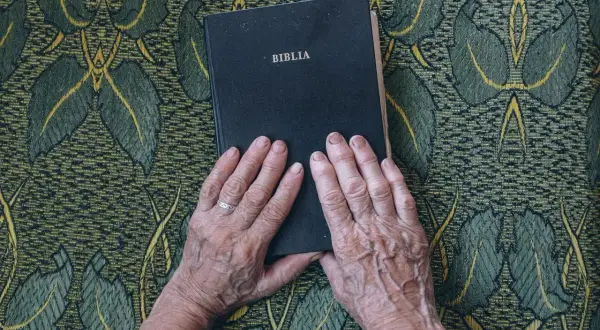 Dłonie starszej osoby spoczywają na Biblii. To symboliczne ujęcie, które może nawiązywać do świadectw nawrócenia znanych osób.