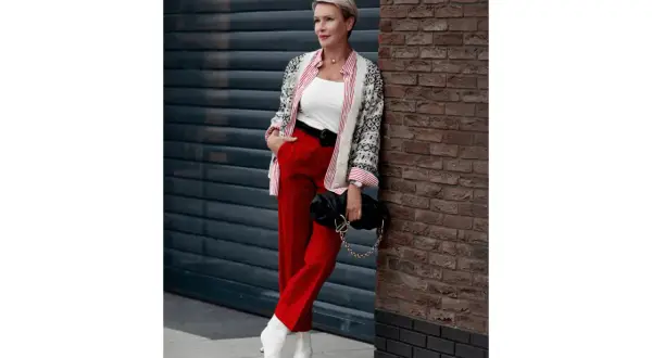 Elegancka kobieta w czerwonych spodniach damskich, białym topie, wzorzystej narzutce i białych botkach. Stylowa stylizacja na co dzień.