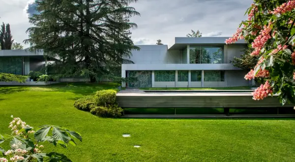Casa moderna rodeada de jardines bonitos, césped verde y flores rosadas.
