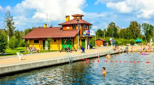Słoneczny dzień nad jeziorem w Węgorzewie. Rodziny odpoczywają na plaży, dzieci kąpią się w wodzie. Idealne miejsce na wakacje z rodziną, oferujące wiele atrakcji dla dzieci.