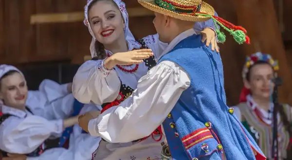 Para tańczy w tradycyjnych strojach ludowych, celebrując muzykę folkową.
