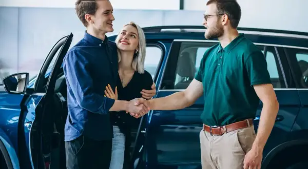 Para młoda uśmiecha się, ściskając dłoń sprzedawcy przy nowym aucie. To ich wymarzony auto w leasing dla osoby prywatnej.