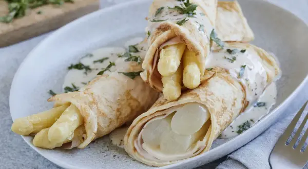 Pfannkuchen mit Spargel und Schinken, übergossen mit einer cremigen Sauce und garniert mit Petersilie.