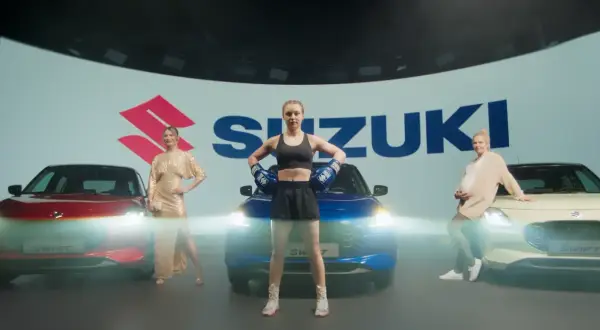 Trzy kobiety obok samochodów Suzuki. Jedna w złotej sukni, druga w stroju bokserskim, trzecia w ciąży. Swift język programowania inspiruje do dynamicznych zmian.