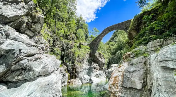 Idyllische Schlucht mit Steinbrücke, ideal für Tessin Wandern. Türkisgrünes Wasser fließt zwischen Felsen.