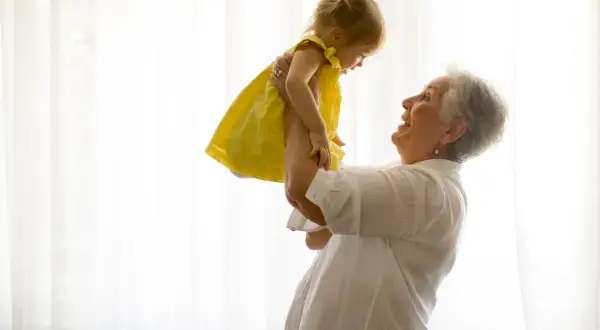 Uśmiechnięta babcia podrzuca w górę wnuczkę w żółtej sukience. Radość i babciowe chwile.