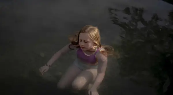 Bambina con capelli biondi immersa nell'acqua scura, un'immagine che evoca la serenità e la purezza, tipica delle opere di Laura Pannack.