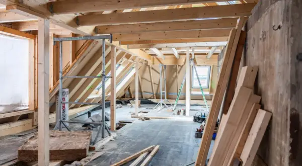 Chantier d'isolation des combles : charpente en bois, rouleaux d'isolant, échafaudages et matériaux de construction.