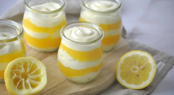 Schichtdessert in Gläsern, perfekt, wenn Sie Zitronenmelisse Creme selber machen möchten. Frische Zitronenhälften liegen daneben.
