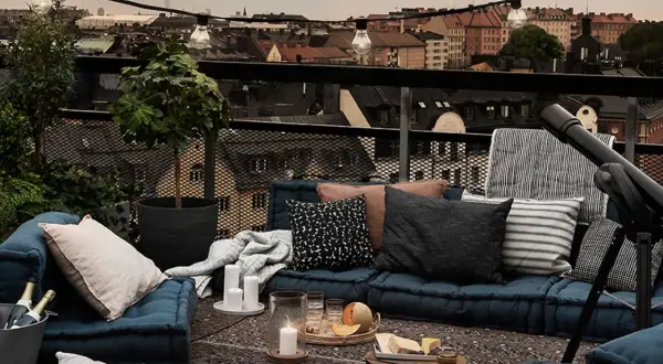 Gemütliches **outdoor wohnzimmer** auf einer Dachterrasse mit Blick auf die Stadt. Blaue Bodenkissen, Decken, Kerzen und eine Lichterkette schaffen Atmosphäre.