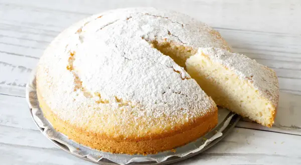 Una soffice torta all'acqua, cosparsa di zucchero a velo, con una fetta tagliata che ne mostra la morbidezza.