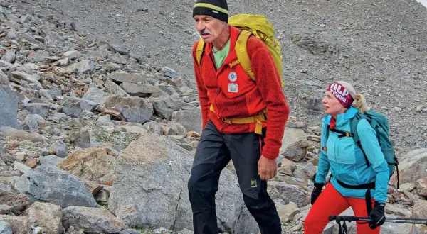 Simon Gietl und eine Frau wandern auf einem felsigen Berghang. Sie tragen Rucksäcke und Wanderkleidung.