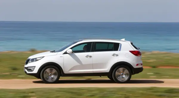 Biały Kia Sportage 2013 jedzie przy błękitnym morzu.