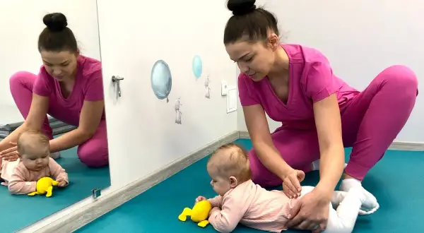 Fizjoterapeutka wspiera niemowlę na brzuchu, ćwicząc jego rozwój. To przykład terapii PNF.
