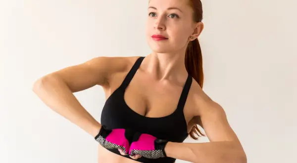Kobieta w sportowym topie i rękawiczkach ćwiczy, pokazując jak ujędrnić piersi.