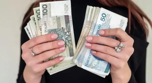 Dłonie trzymające pliki polskich banknotów 100 i 50 zł. Zastanawiasz się, jaka emerytura przy zarobkach 7000 brutto?