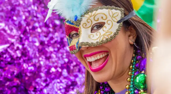 Donna sorridente con maschera di carnevale e perline colorate. L'etimologia di carnevale, "addio alla carne", si riflette nella gioia sfrenata.