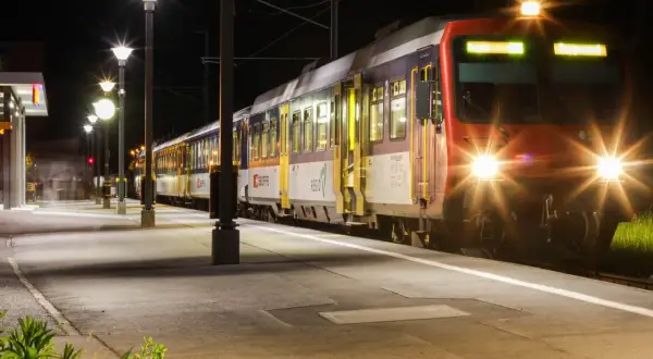 Ein Zug mit roten und blauen Waggons steht nachts am Bahnsteig. Die Scheinwerfer leuchten hell. Ein perfekter Start für eine Reise mit Interrail Italien.