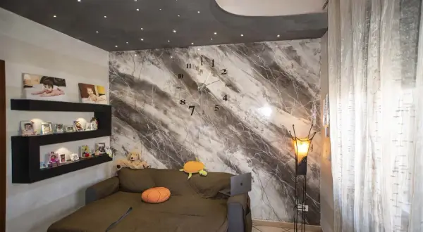 Soggiorno con divano, orologio a muro e una parete con una suggestiva texture pittura effetto marmo.